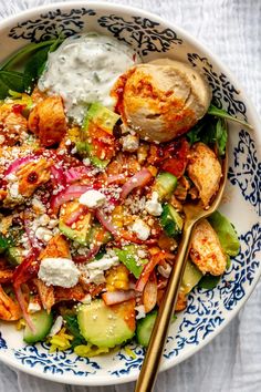 a bowl filled with salad and dressing on top of a white table cloth next to a gold spoon