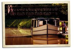 two people are standing on the deck of a boat in the water near a bridge