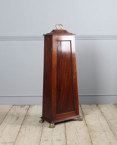 an old wooden grandfather clock on display in a room with wood floors and gray walls