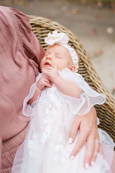 a woman holding a baby wearing a white dress and a pink shirt on her lap