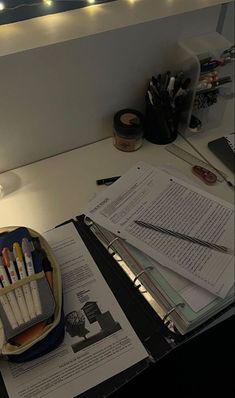 an office desk with pens, pencils and papers on it next to a lamp