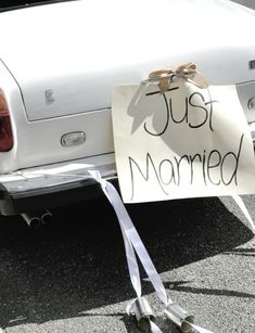 a sign that says just married next to a white car with a ribbon tied around it