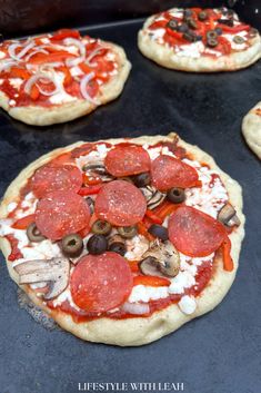 four pizzas with pepperoni, olives and mushrooms on top of an oven