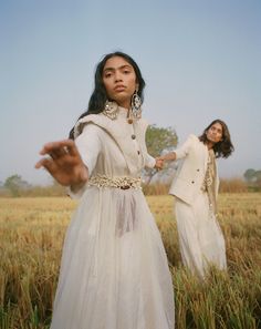 two women standing in a field with their hands out and one woman wearing a white dress