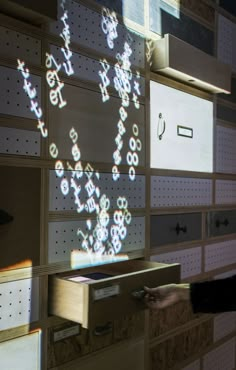 a person standing in front of a wall with lots of drawers and letters on it