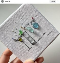 a hand holding up a card with three glasses on it, one is blue and the other is green