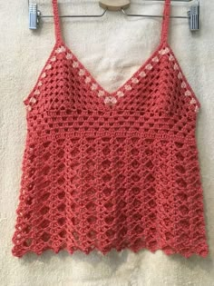 a red crocheted top hanging on a clothes hanger next to a white towel