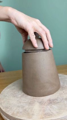 a person's hand is on top of a clay pot sitting on a table