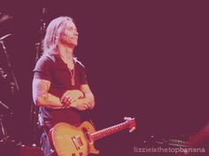 a man with long hair playing an electric guitar in front of other instruments on stage