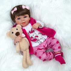 a baby doll is holding a teddy bear on a fluffy white blanket with a pink outfit