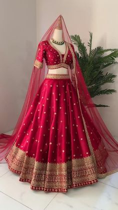 a red lehenga with gold work on the top and bottom, is displayed in front of a plant