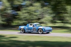 an old blue race car driving down the road with trees in the backgroud