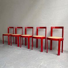 four red chairs sitting next to each other in front of a white wall and cement floor