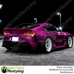 a purple sports car parked in front of a parking lot at night with its lights on