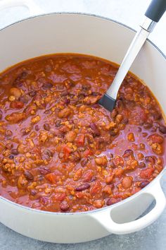 a white pot filled with chili and beans on top of a gray counter next to a black spatula