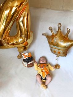 a baby is laying next to some balloons and a cake with a crown on it