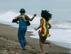 two people are running on the beach near the ocean and one is holding a cell phone