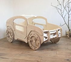 a wooden toy car sitting on top of a hard wood floor next to a tree