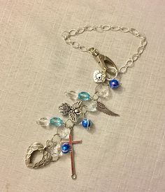 a cross with blue glass beads and charms on a silver chain bracelet that is laying on top of a white cloth