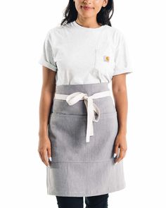 a woman standing in front of a white background wearing an apron and smiling at the camera