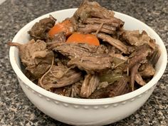 a white bowl filled with meat and carrots on top of a counter next to a marble table