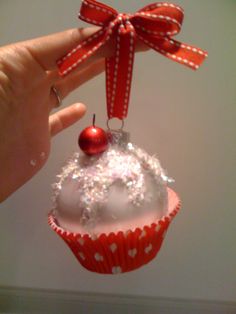 a hand holding a cupcake ornament with a red bow