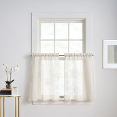 a window with white curtains and flowers on a small table in front of the window