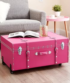 a pink suitcase sitting on top of a hard wood floor next to a gray couch