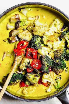 a pan filled with broccoli, cauliflower and red peppers next to a wooden spoon