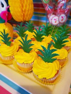 pineapple cupcakes with yellow frosting and green leaves are on a tray