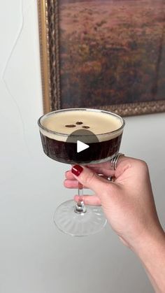 a person holding a wine glass in front of a painting on the wall with red nail polish