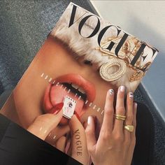 a woman is holding up a magazine with her nails on it and wearing gold jewelry