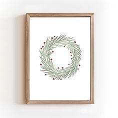 a christmas wreath with red berries and green leaves on white paper in a wooden frame