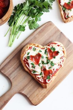 a heart shaped pizza sitting on top of a wooden cutting board