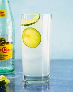 a glass filled with ice and lime next to a bottle