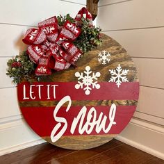 a wooden sign that says let it snow on the side of a house with red and white bows