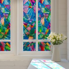 a vase filled with white flowers sitting next to two stained glass windows in a room