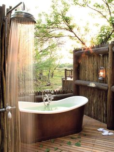 an outdoor shower with bamboo walls and flooring in front of a bathtub surrounded by trees