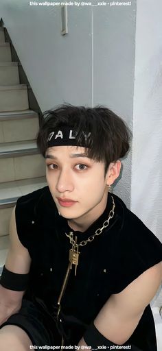 a young man wearing a black shirt and gold chain around his neck sitting on the stairs