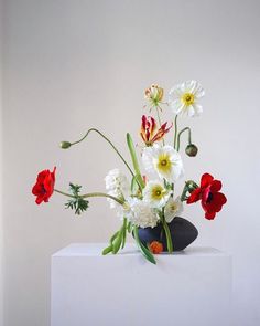 a vase filled with white and red flowers on top of a table next to a wall