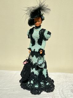 a crocheted doll wearing a dress and hat with black hair, holding an umbrella