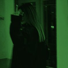 a woman with long blonde hair standing in a dark room holding a cell phone up to her ear