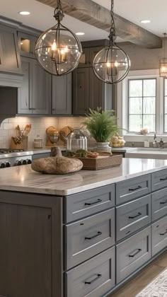 a large kitchen with gray cabinets and marble counter tops, two chandeliers hanging from the ceiling