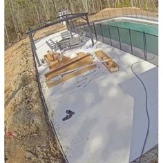 an aerial view of a pool being built in the middle of a wooded area with fencing around it