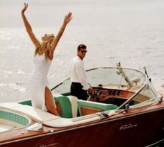 a man and woman standing on the back of a boat in the water with their arms up