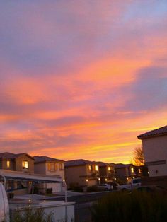 the sun is setting over some houses and parking lots in front of them,