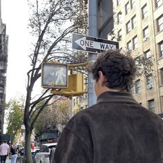 a man standing next to a traffic light under a one way sign on a city street