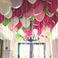 many balloons are hanging from the ceiling in front of a window with pink, green and white streamers