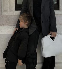 a man in a suit and tie standing next to a little boy with a handbag