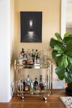 a bar cart with liquor bottles and glasses on it next to a potted plant